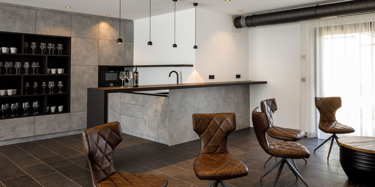 Modern kitchen with gray cabinets, brown leather chairs, hanging lamps and black shelves with glassware.